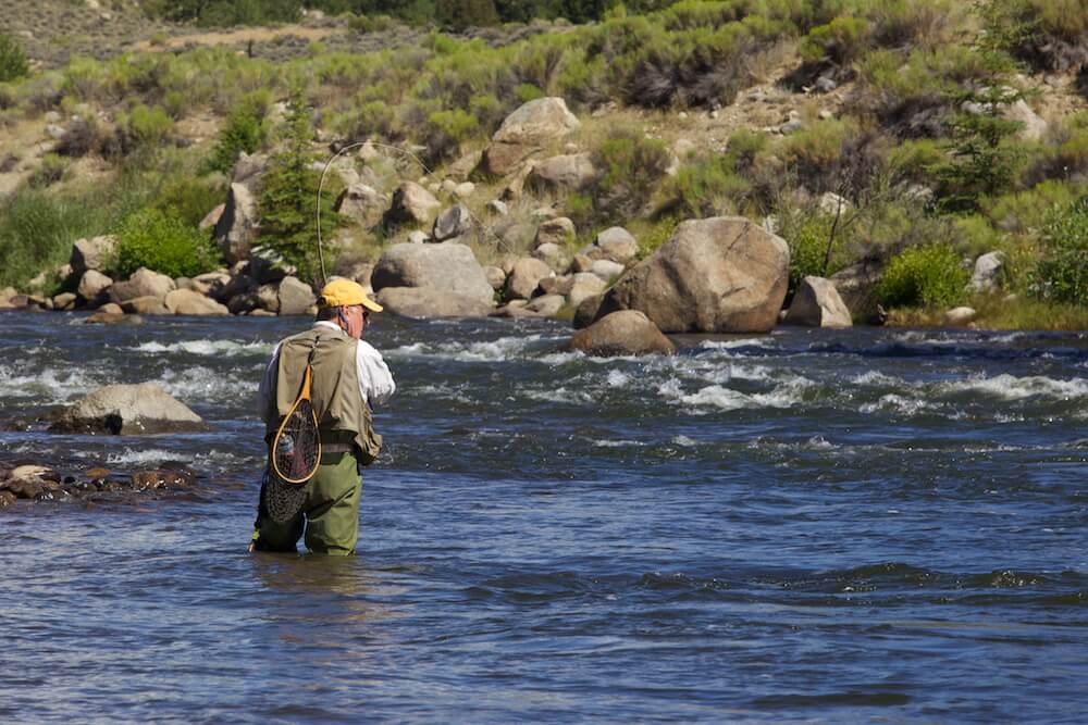 A man wading in a river with a fly rod