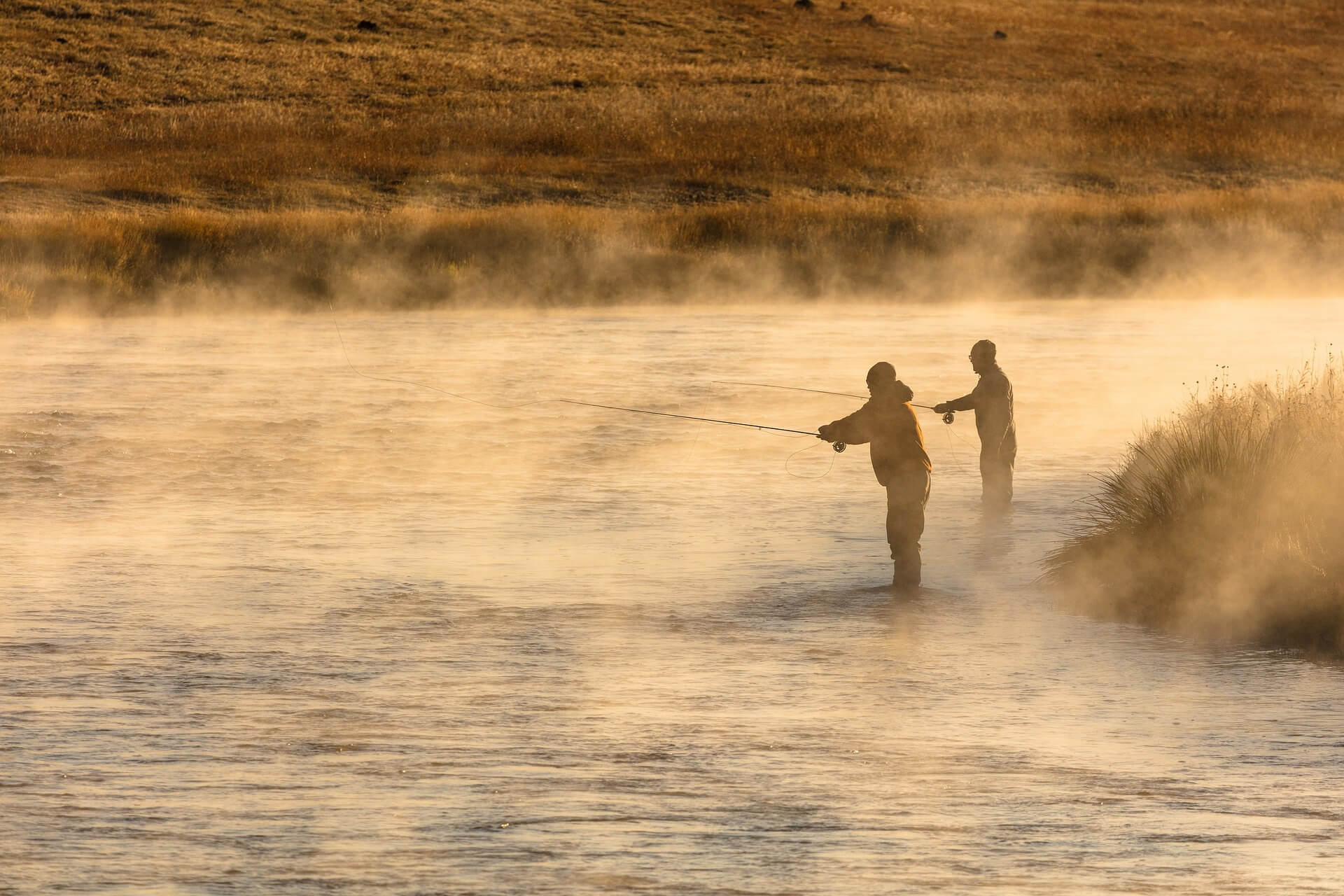Two people fly fishing during golden hour with a steaming river