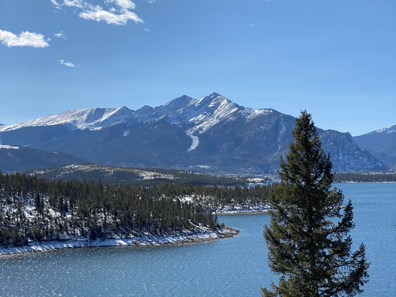 Lake Dillon during the winter with a mountain in a background and a tree in the foreground