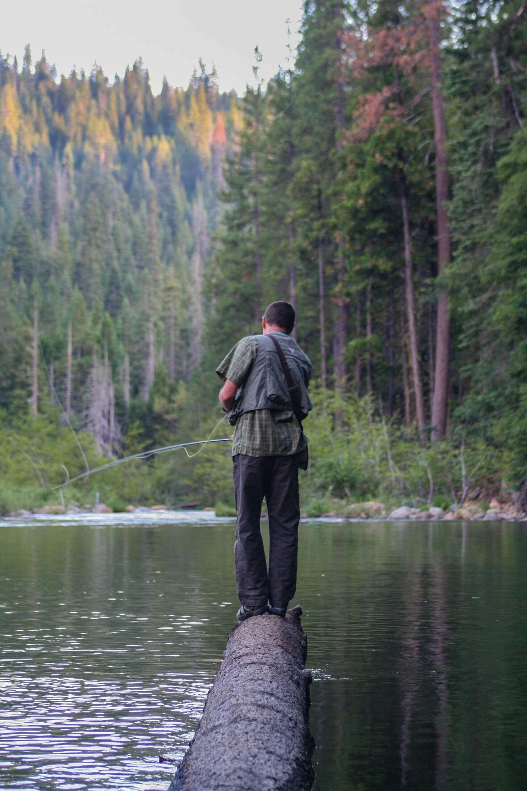 man standing on log fly fishing