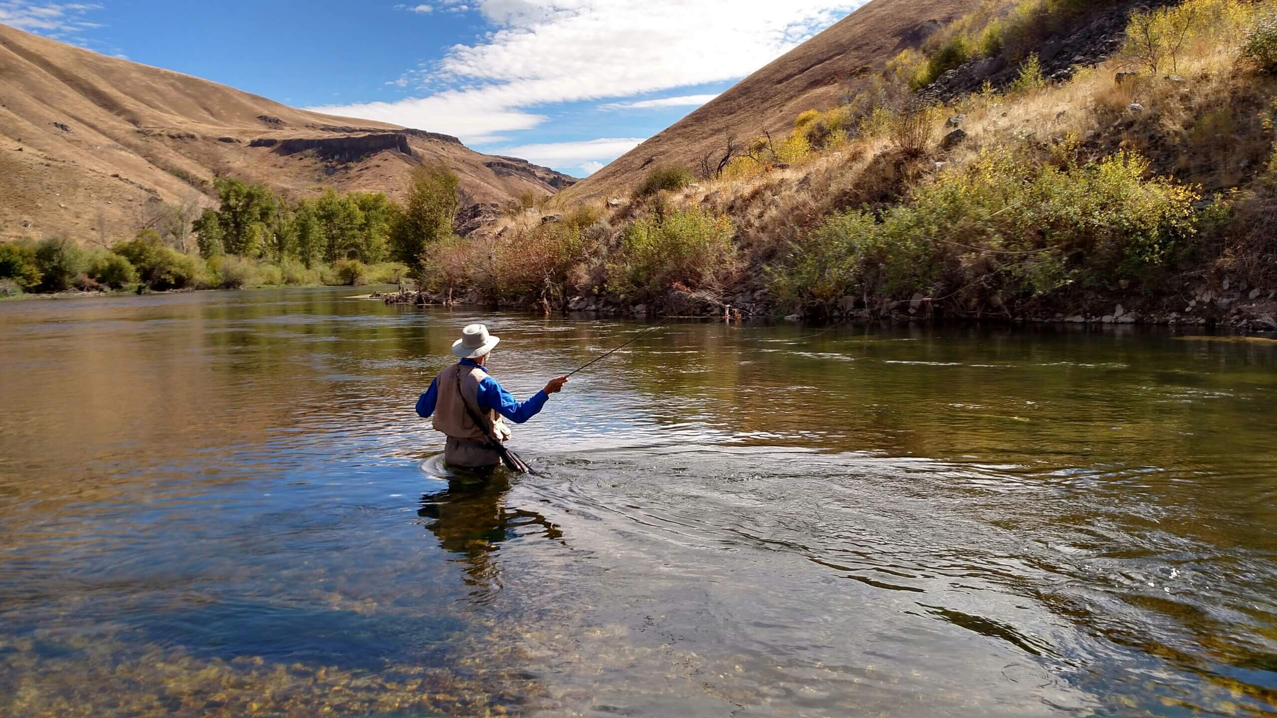 man fly fishing in middle of river