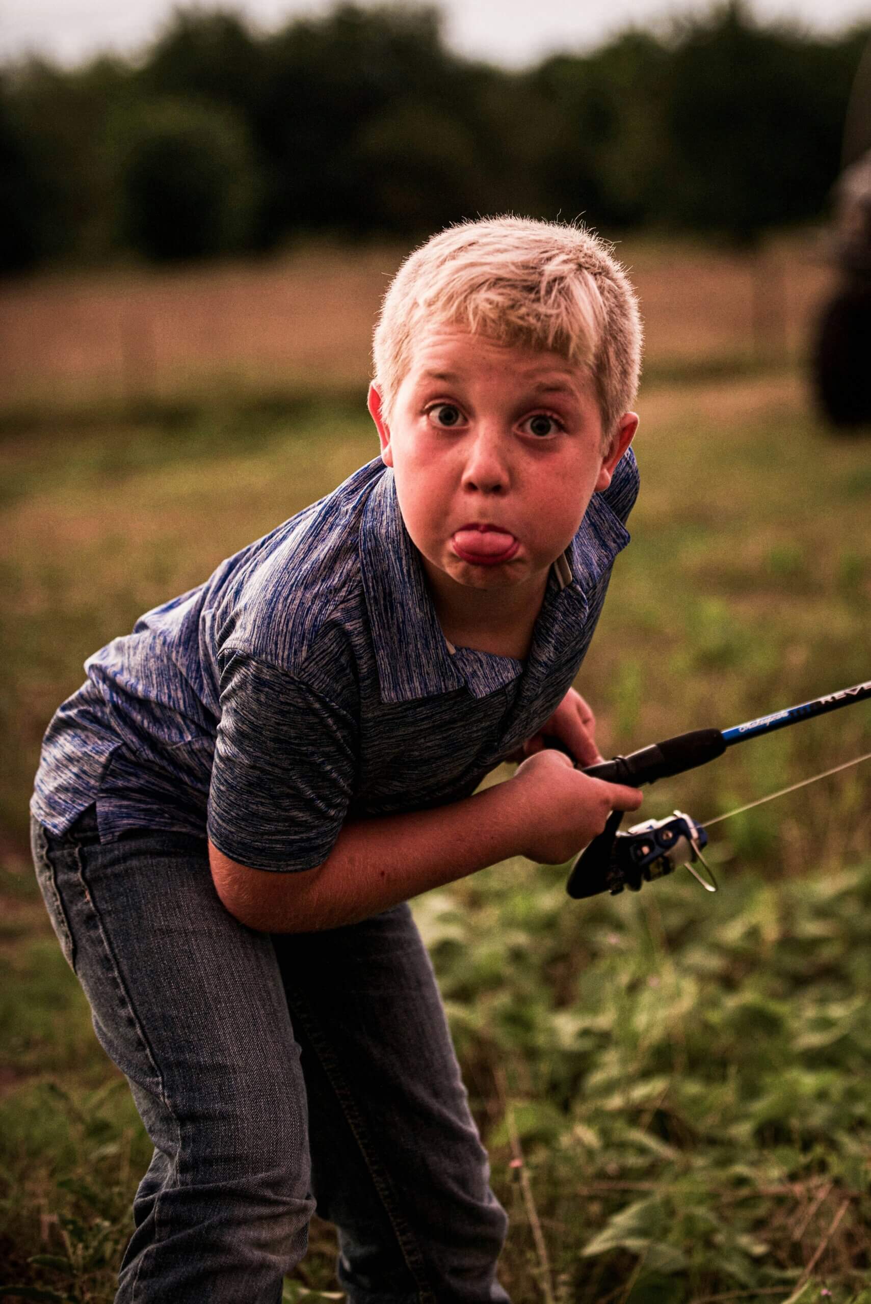 kid sticking out tongue holding fishing pole